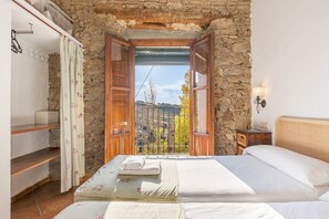 A bedroom with a stone wall, a bed with white linens, a wooden nightstand, and a view through an open door.