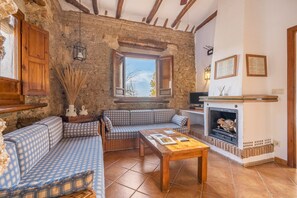 Una habitación rústica con pared de piedra, un conjunto de sofá de madera, una chimenea y una ventana con vistas.