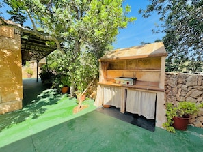 Un área de cocina al aire libre con pared de piedra, encimera de madera y una parrilla.