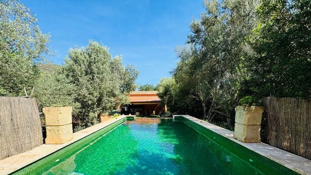 A rectangular swimming pool with clear water, surrounded by trees and a building with a red roof in the background. - Country House 'Can Conill Llucmajor' with Mountain View, Wi-Fi and Air Conditioning (Illes Balears)