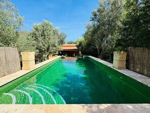 Une piscine rectangulaire à l’eau claire, entourée d’arbres, avec un bâtiment au toit rouge en arrière-plan.
