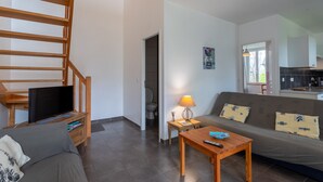 A modern living room with a sofa, a coffee table, a TV, and a staircase. - La Maison de Tété – Charming Cottage near Lourdes, Private Terrace, Garden, WiFi (Artigues)