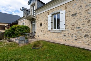 A stone house with a patio, a small garden, and a table with chairs.