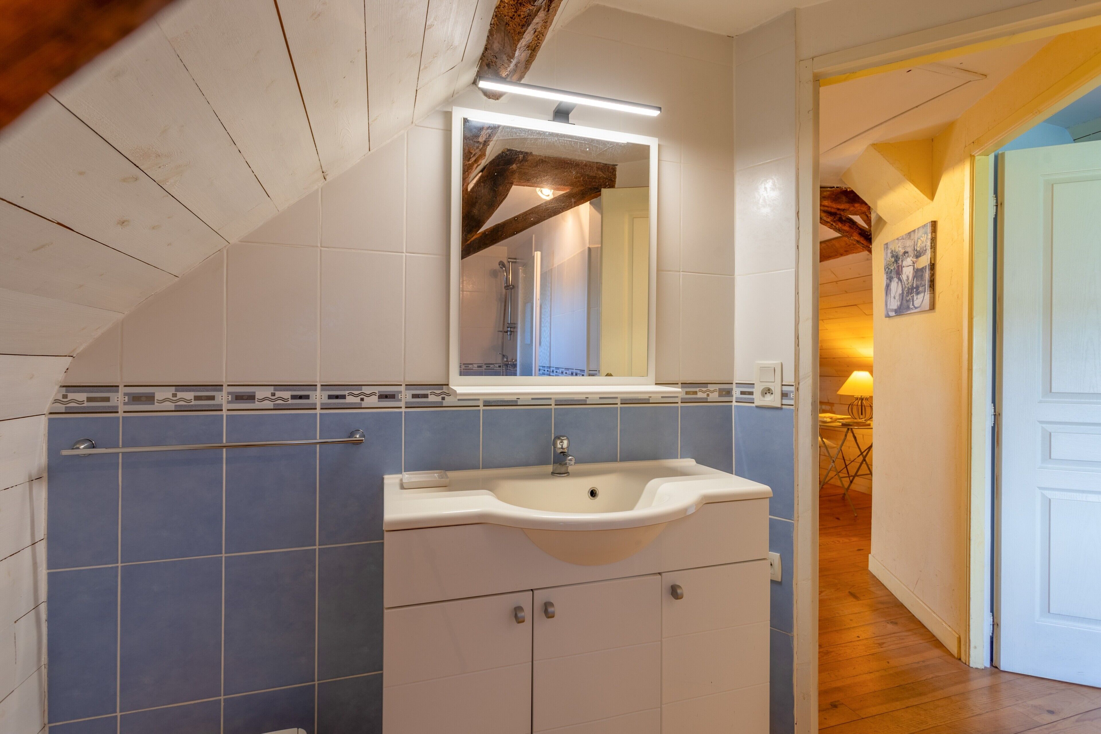 A bathroom with a white sink, blue tiles, a wooden ceiling, and a mirror above the sink.