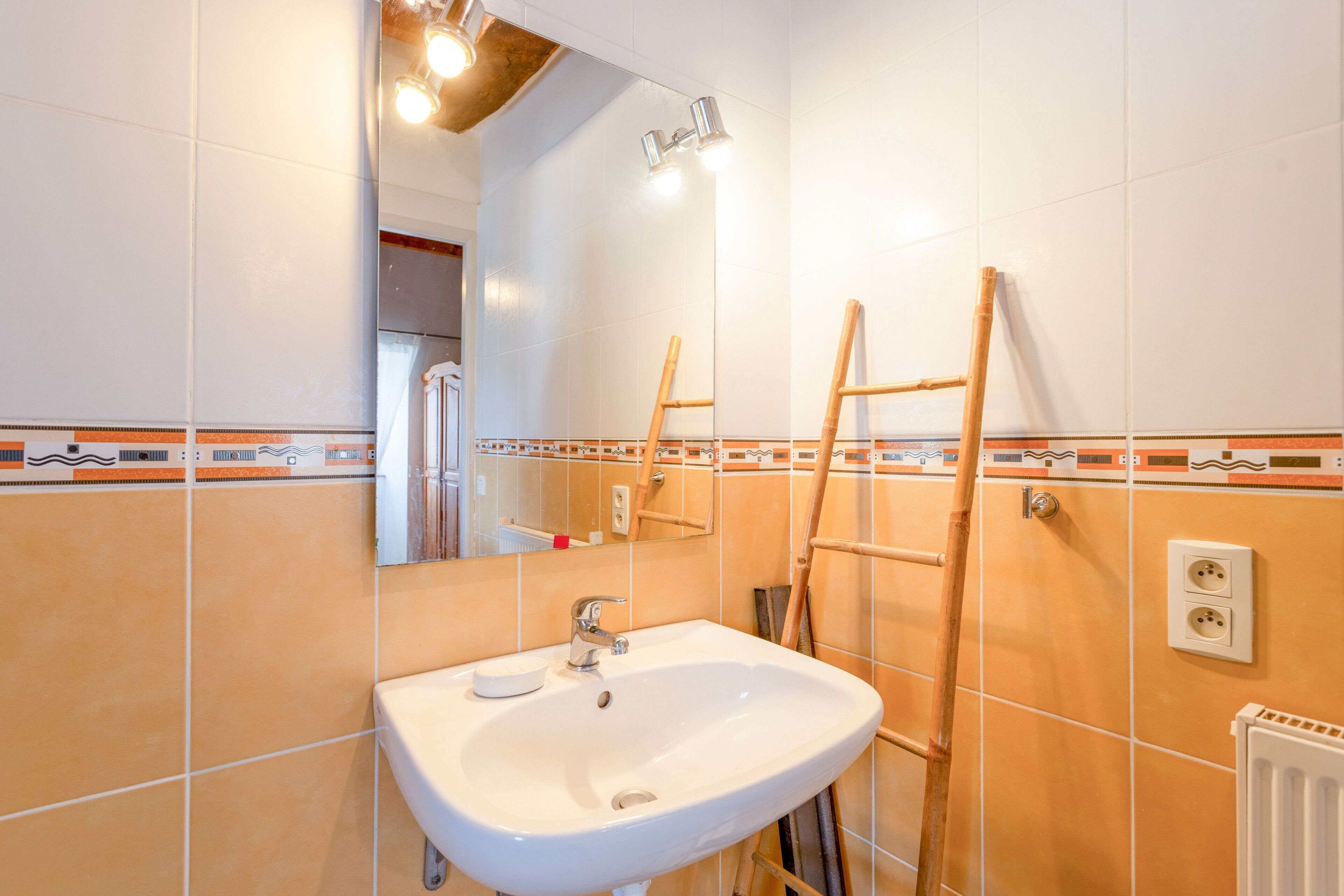 Een badkamer met een wit wastafel, spiegel en betegelde muren.