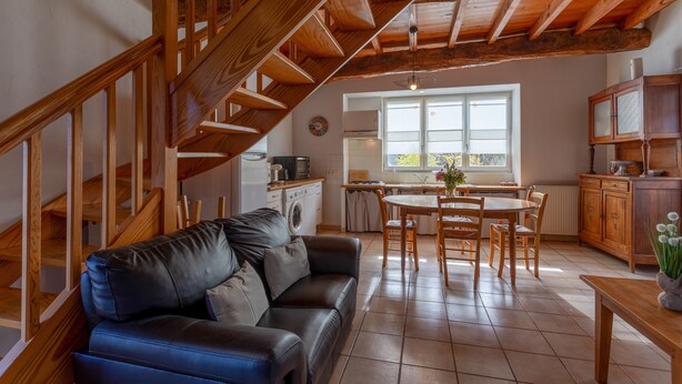 A spacious living area with a wooden staircase, a dining table with chairs, a kitchen area, and a large window. - La Bergerie – Cozy House 5 min from Lourdes, Private Garden, Terrace, WiFi (Adé)