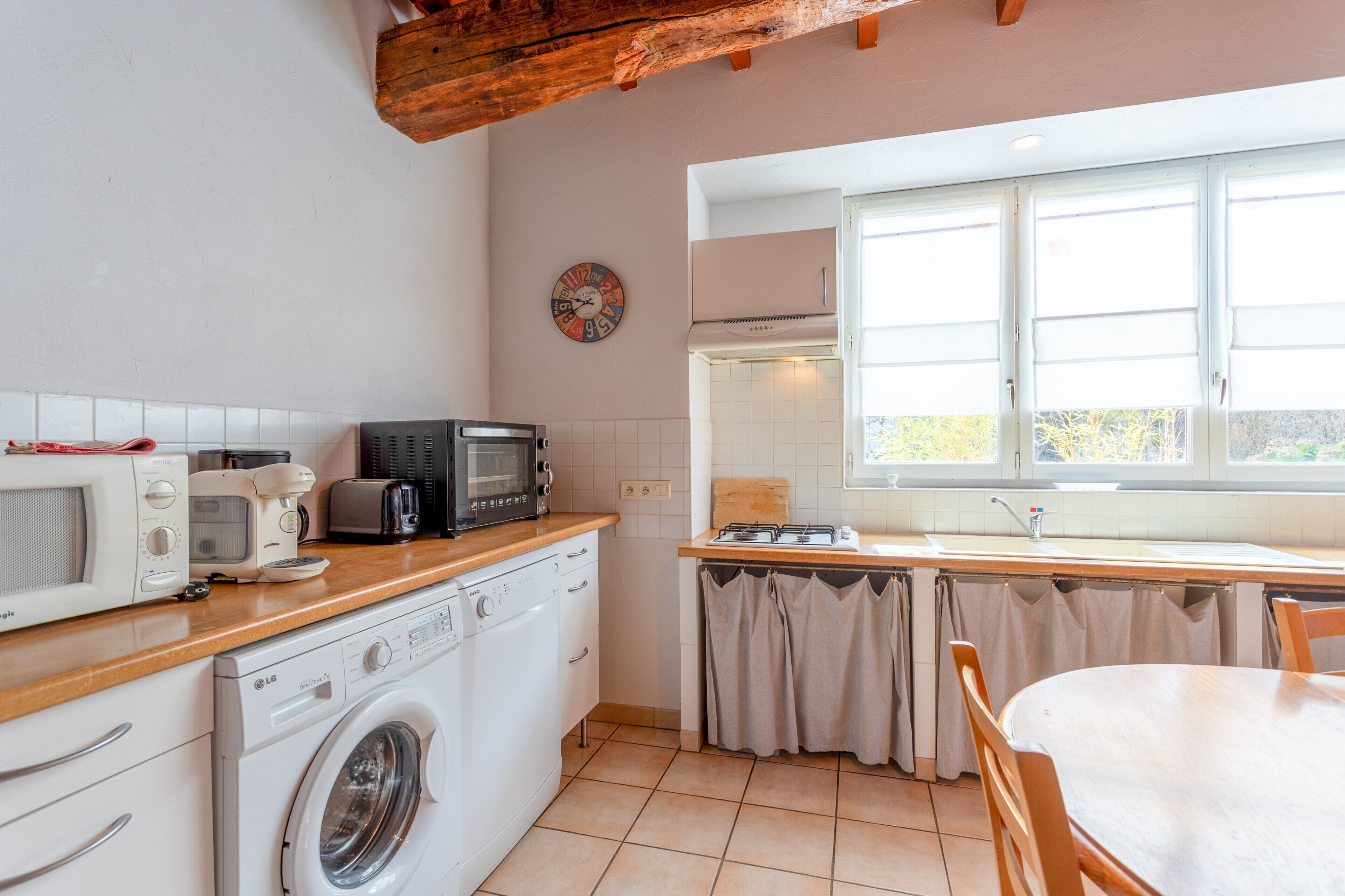 Una cocina compacta con lavadora, microondas, tostadora y un reloj en la pared.
