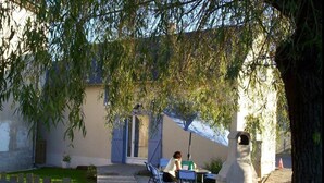 A courtyard with a table and chairs, a stone structure, and a building with blue shutters. - La Bergerie – Cozy House 5 min from Lourdes, Private Garden, Terrace, WiFi (Adé)