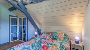A bedroom with a sloped ceiling, a bed with a floral bedspread, two bedside lamps, and a wooden nightstand with a lamp. - La Bergerie – Cozy House 5 min from Lourdes, Private Garden, Terrace, WiFi (Adé)