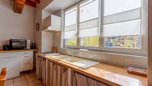 A kitchen with a stove, sink, and window overlooking a garden. - La Bergerie – Cozy House 5 min from Lourdes, Private Garden, Terrace, WiFi (Adé)