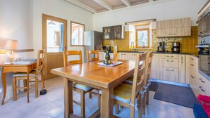 Una cocina con armarios de madera, una mesa de comedor, sillas, una cafetera y un refrigerador.