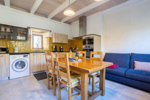 Een kleine keuken met houten kastjes, een inbouw wasmachine en een eethoek met een tafel en stoelen.