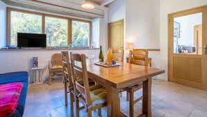 Un comedor con una mesa de madera, sillas, un televisor y una ventana con vista a árboles.