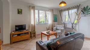 Una sala de estar con televisor, mueble de madera para equipo multimedia, sofá, mesa de centro y una silla.