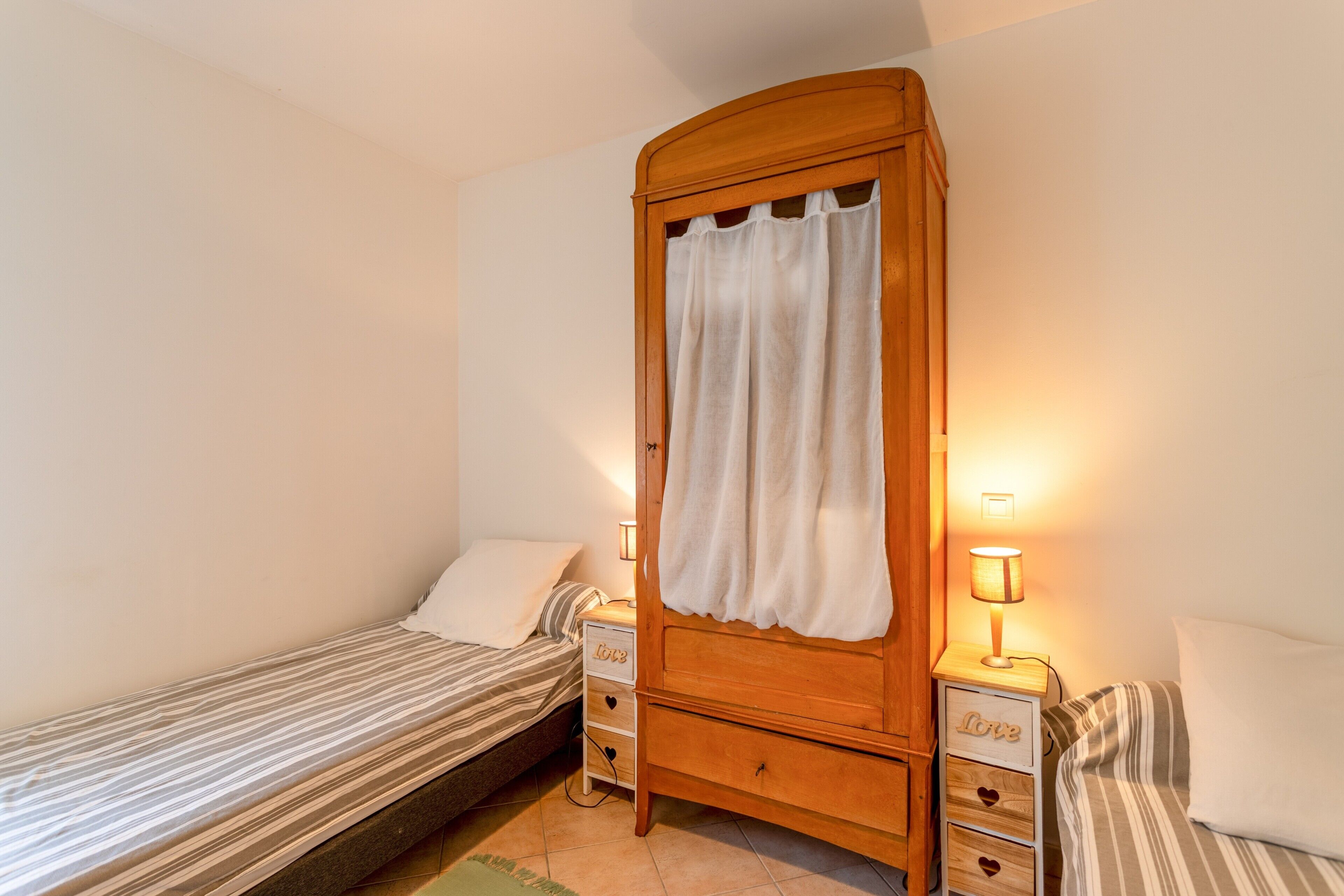 Un dormitorio con dos camas individuales, un armario de madera, lámparas de noche y una mesita de noche con lámpara.