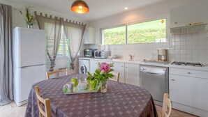 Cocina compacta con refrigerador, microondas, estufa y lavavajillas. Hay una mesa de comedor con un florero y una bandeja con tazas y tetera.