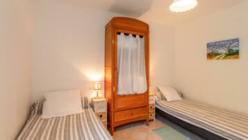 A bedroom with two single beds, a wooden wardrobe, a nightstand with a lamp, and a painting on the wall.