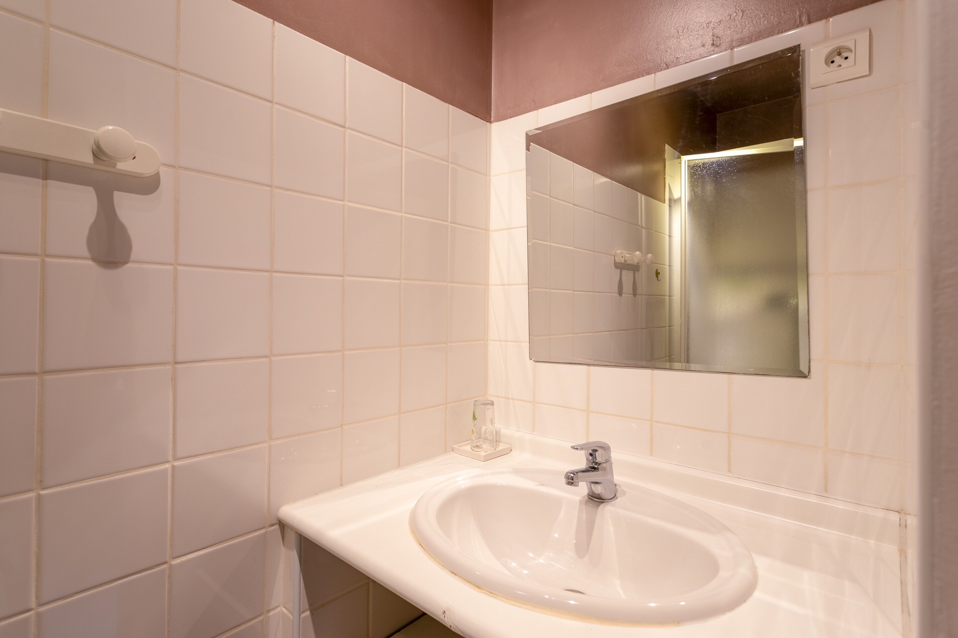 A bathroom with white tiles, a sink, a mirror, and a towel rack.