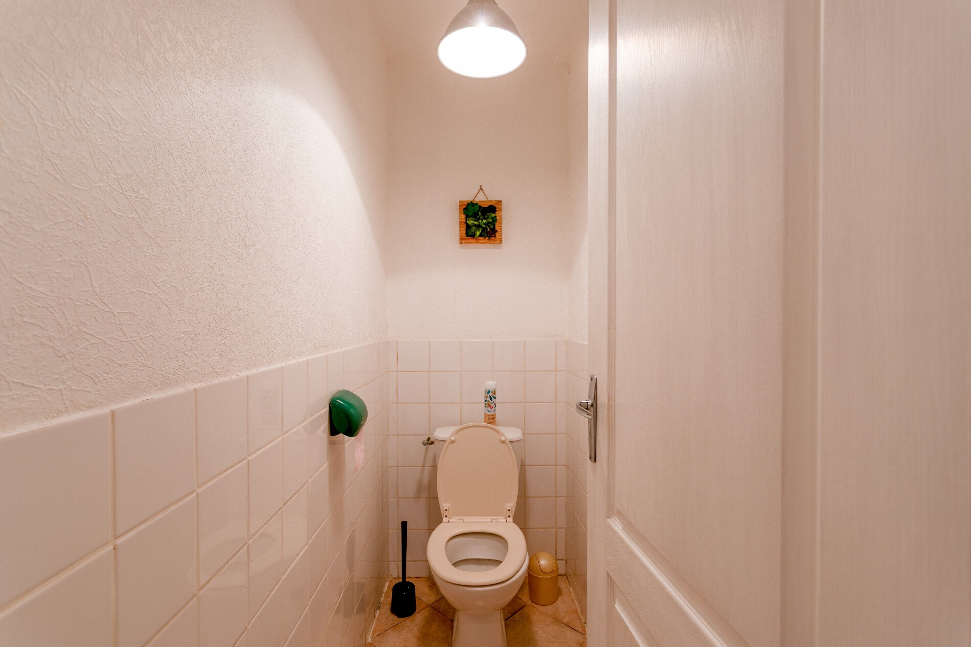Ett litet, rent badrum med en toalett, en handtork och en papperskorg.