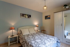 Un dormitorio con cama, dos lámparas de noche, una mesita de noche, una silla, un armario y dos cuadros en la pared.