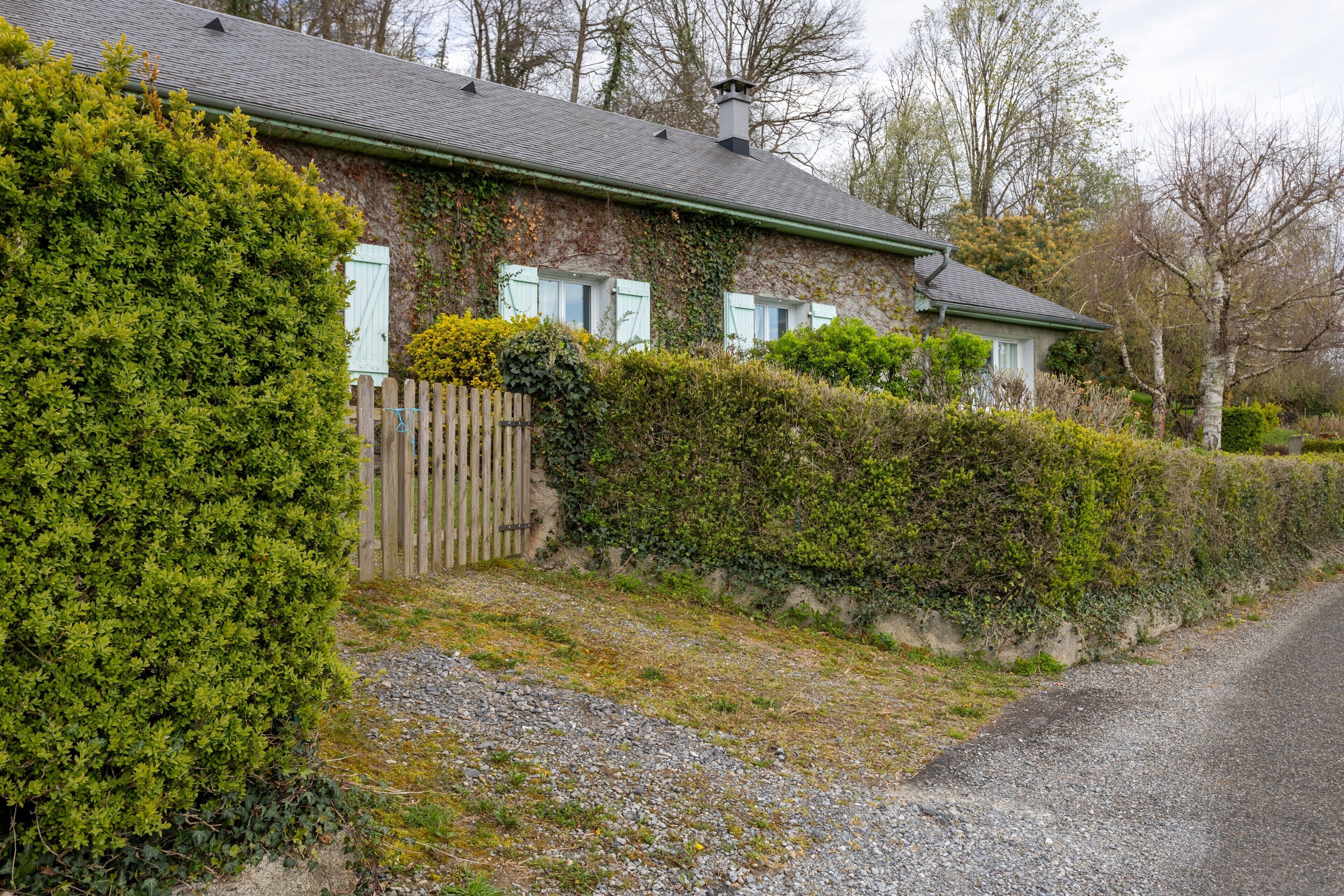 A stone house with a sloped roof, a wooden fence, and a gravel driveway.