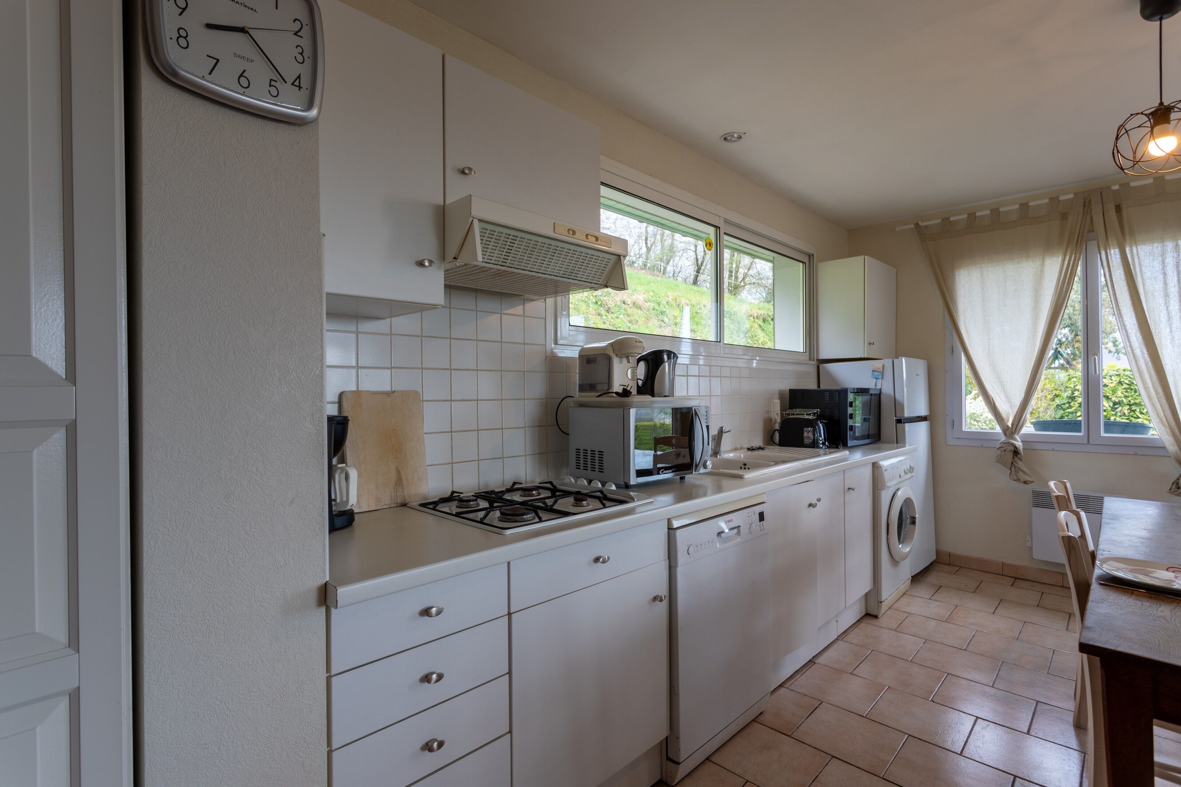 A kitchen with a gas stove, microwave, dishwasher, and a clock on the wall.