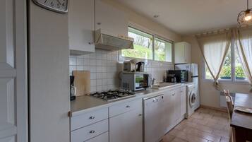 A kitchen with a gas stove, microwave, dishwasher, and a clock on the wall.
