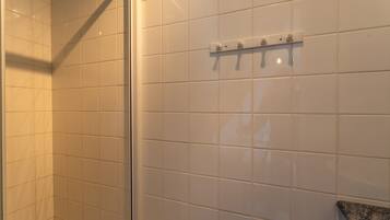 A tiled bathroom with a shower area, a towel rack, and a corner with a glass door.
