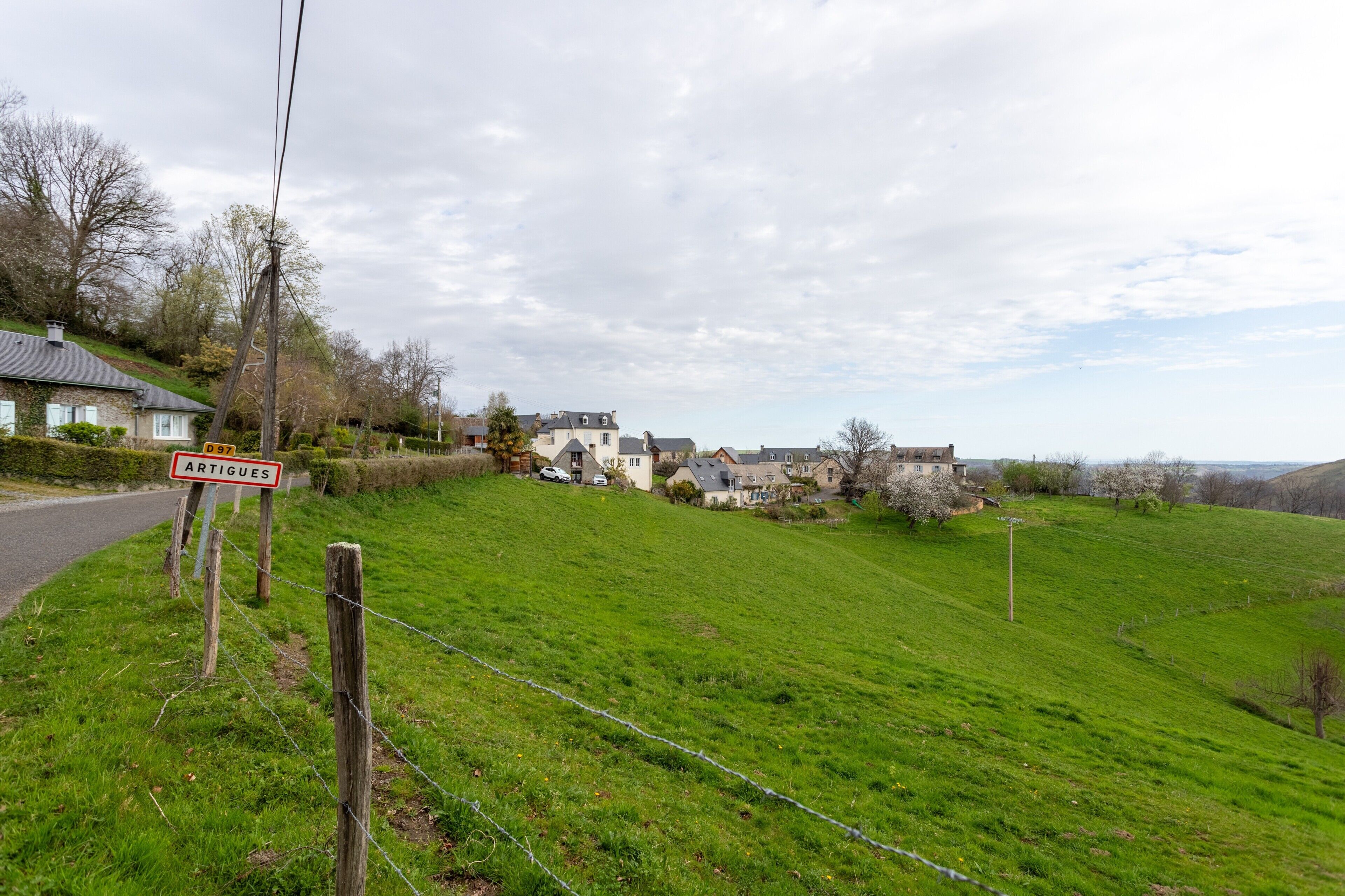 Ländliche Landschaft mit Häusern, einem Schild mit der Aufschrift 'ARTIGUES' und einer Straße.