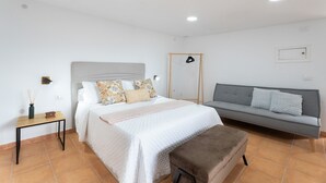 A bedroom with a bed, a sofa, a small table, and a bench.