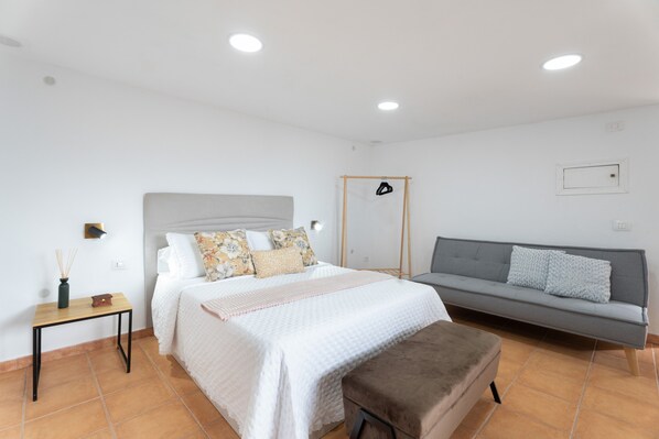 A bedroom with a bed, a sofa, a small table, and a bench.
