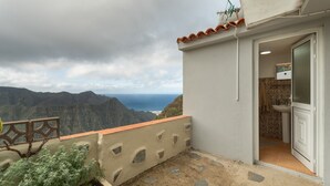 A balcony with a view of mountains and the sea, a small sink, and a door leading to a bathroom.
