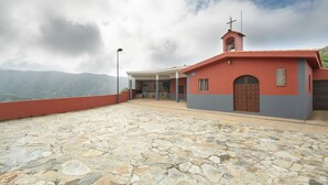 A church with a red and grey exterior, a bell tower, and a stone-paved courtyard.