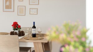 A dining table with a wine bottle, glasses, pine cones, and a vase of red flowers.