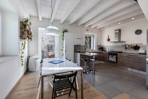 Une cuisine moderne avec une table blanche, des chaises en bois, un luminaire suspendu et un four en acier inoxydable.