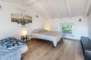 Une chambre à coucher avec un lit, une table de chevet avec une lampe, une fenêtre donnant sur un beau paysage et une œuvre d’art représentant un paysage urbain accrochée au mur.
