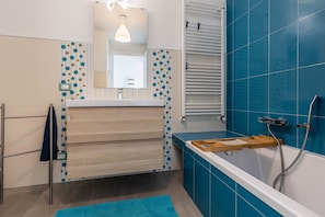 Une salle de bain avec une baignoire, un porte-serviettes, un meuble en bois et un mur recouvert de carreaux bleus.