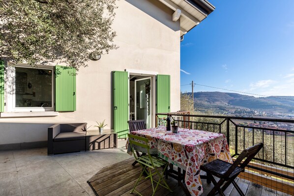 Un balcon avec une table et des chaises, une vue sur la campagne et un bâtiment aux volets verts.