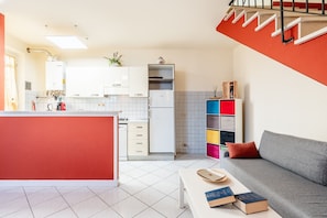 A modern kitchen with white cabinets, a refrigerator, and a dining area with a white table and books.