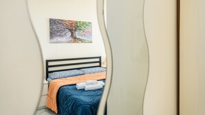 Una cama con colcha azul, manta naranja y almohada blanca.