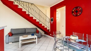 Una sala de estar con una escalera, un sofá, una mesa de centro y un comedor con sillas y una mesa.