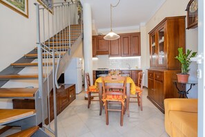 Una cocina con armarios de madera, una mesa de comedor con sillas, una escalera y una planta en maceta.