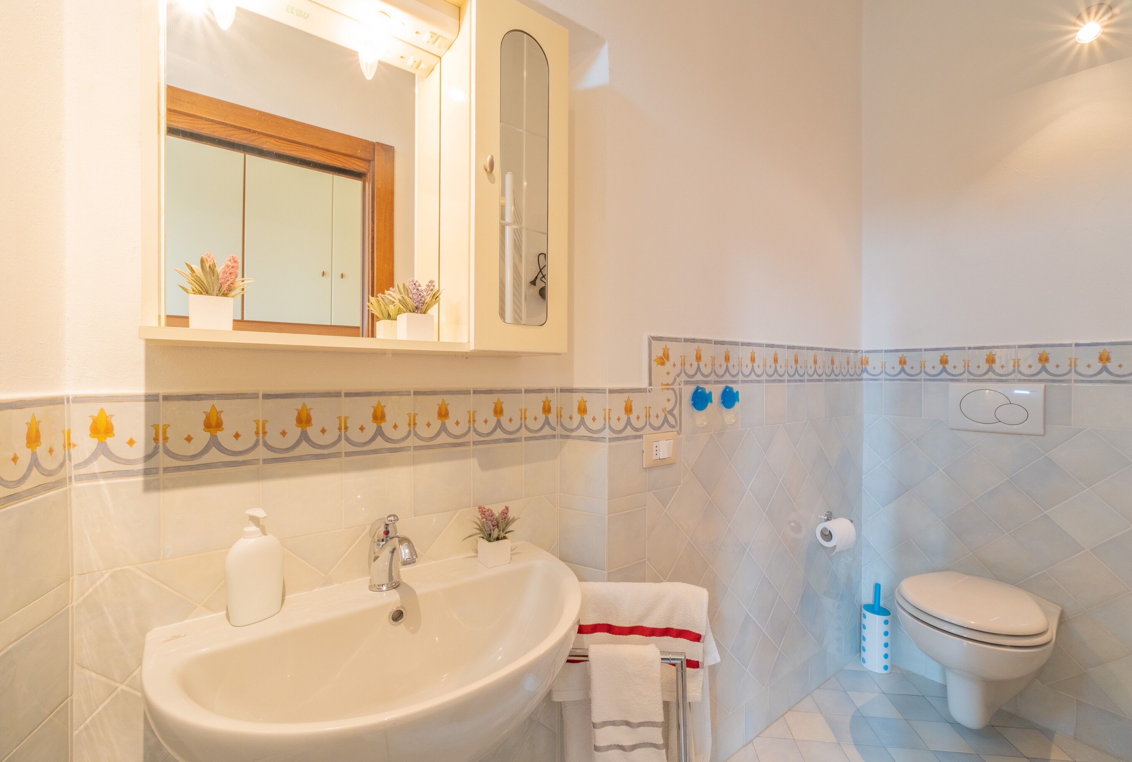 Une salle de bain équipée d’un lavabo, d’un miroir, de toilettes et de carreaux décoratifs.