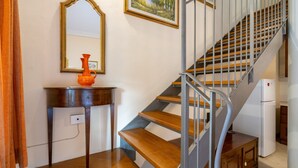 Una escalera con escalones de madera y barandillas de metal, una mesa de madera con un jarrón, un espejo y un cuadro en la pared.