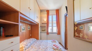 Un dormitorio con cama, armario, radiador, ventana con cortinas y un muro con cuadros enmarcados.