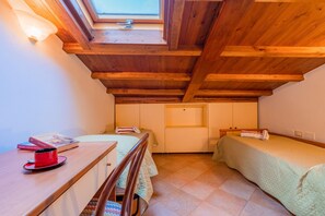 Una habitación pequeña y acogedora con techo inclinado, tragaluz, cama, escritorio y una silla.
