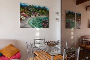 Un comedor con mesa de vidrio y sillas de metal, un sofá con cojines y dos cuadros en la pared.