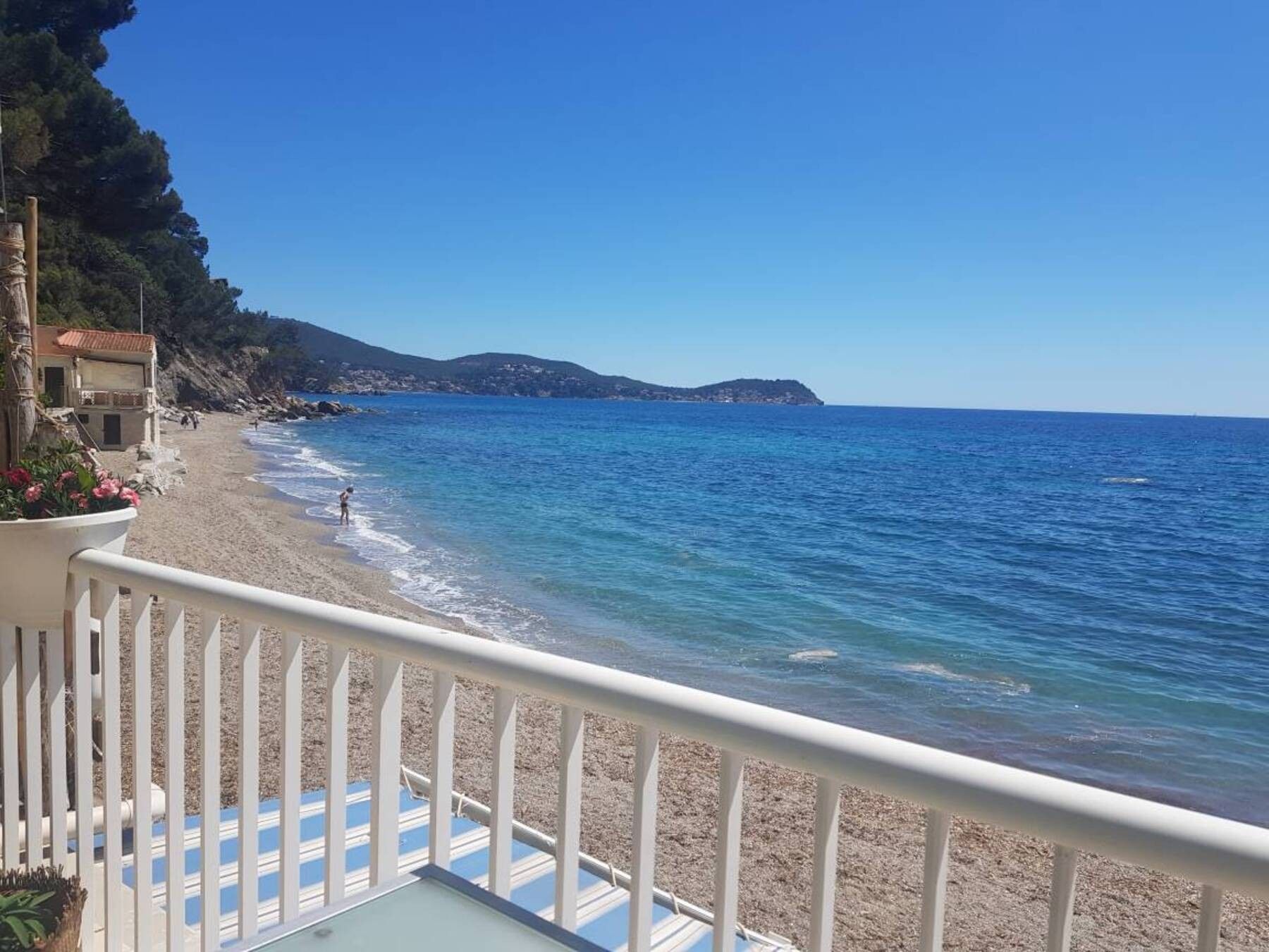 Une plage offrant une vue dégagée sur la mer, un bâtiment situé à gauche et un balcon doté d’une balustrade.