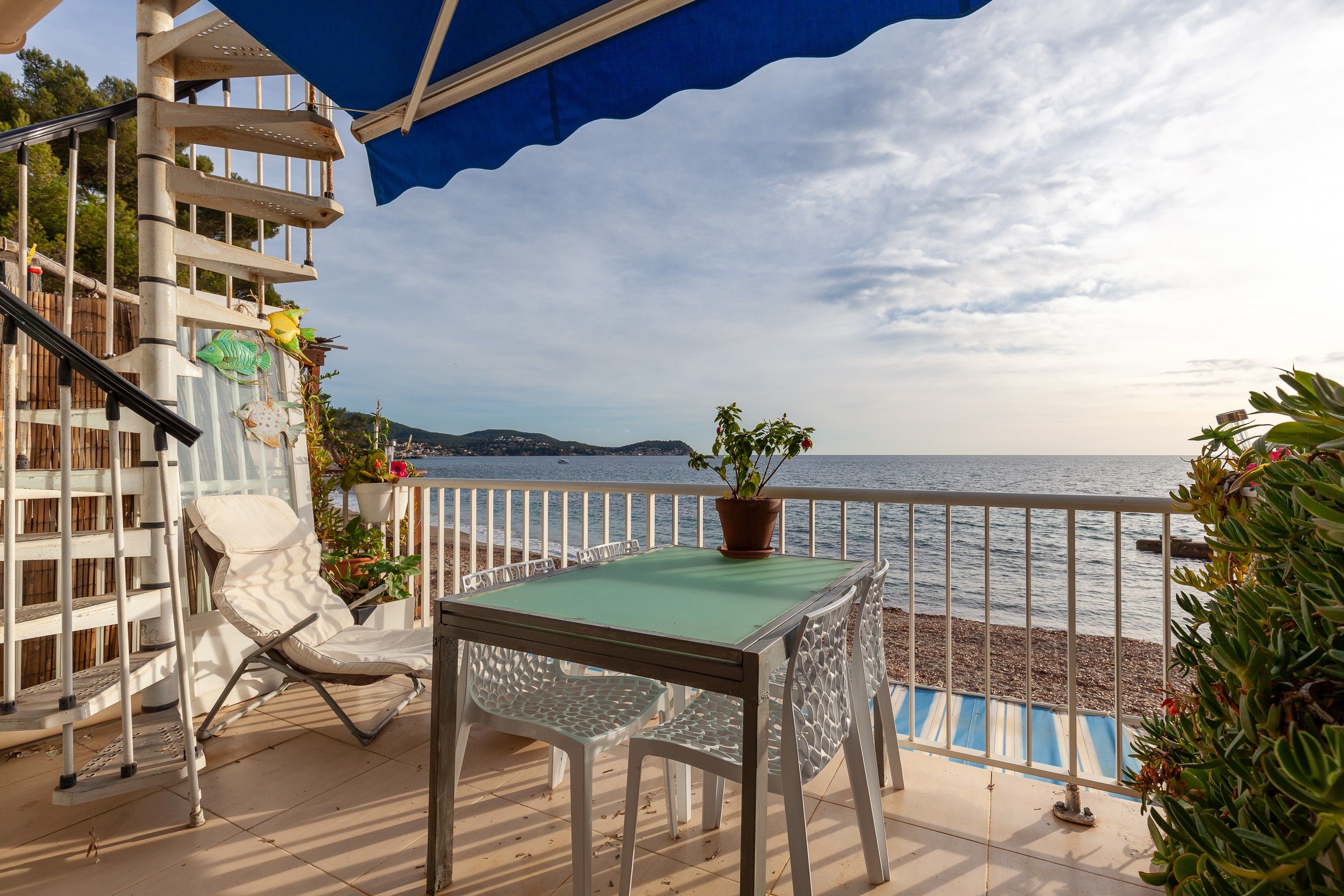 A balcony with a table and chairs, overlooking a body of water and a distant coastline.