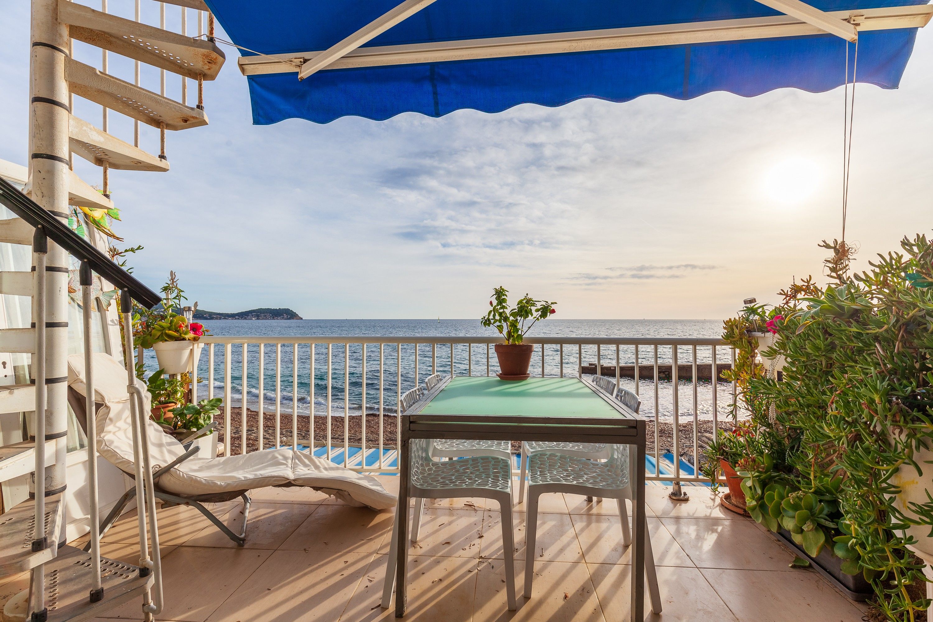Un balcon avec une table et des chaises, donnant sur une plage et la mer.